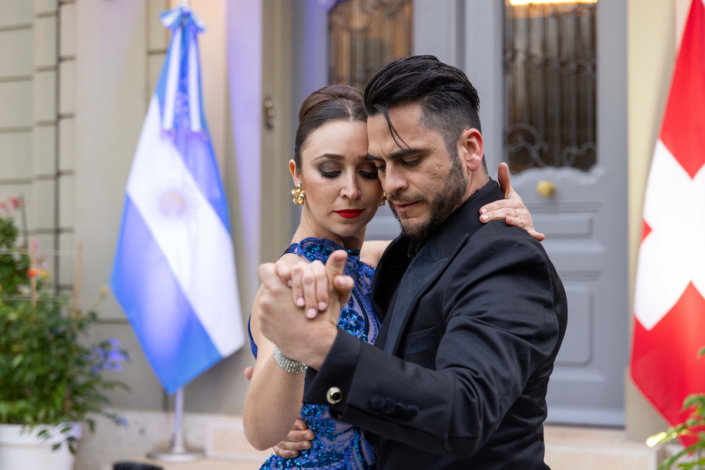 A man and a woman dance in front of flags.