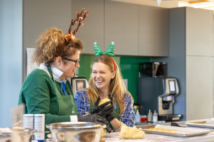 Two women with reindeer antlers in a kitchen.