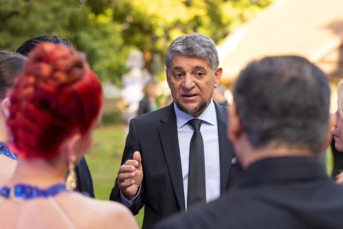 Ein Mann im Anzug unterhält sich bei einer Veranstaltung im Freien mit Menschen.