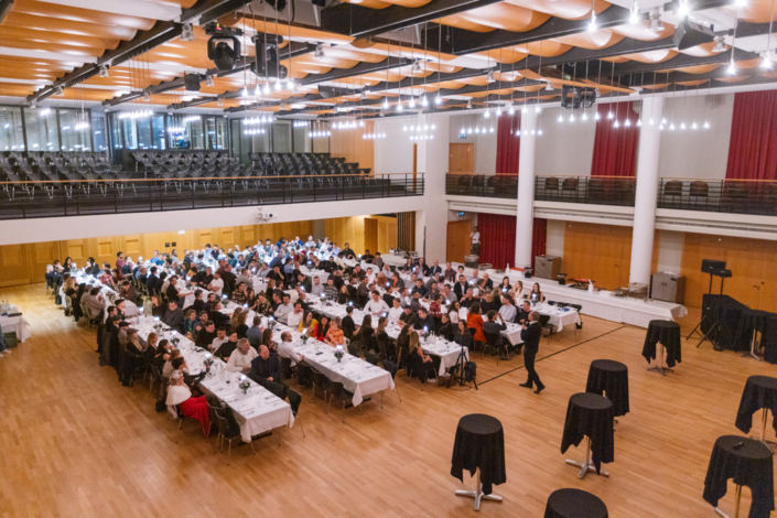 A large hall with lots of people sitting at tables.