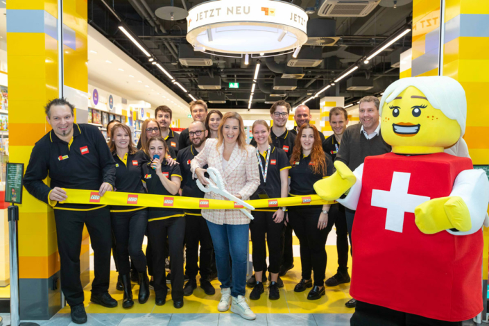 A group of people cut a ribbon in front of a Lego store.