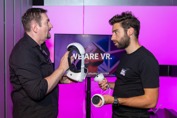 Zwei Männer stehen nebeneinander und halten ein VR-Headset in der Hand.