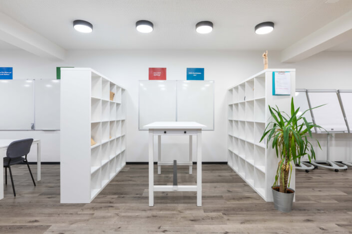 A white office with shelves and a plant on the floor.