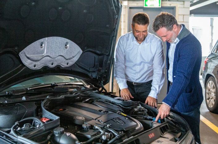 Zwei Männer schauen auf die Motorhaube eines Autos.