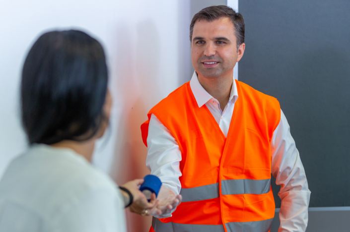 A man in an orange vest shakes hands with a woman.