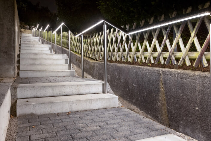 A staircase illuminated at night with a fence in the background.