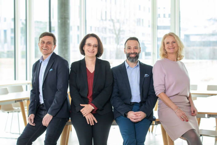 Four business people pose for a photo in an office.