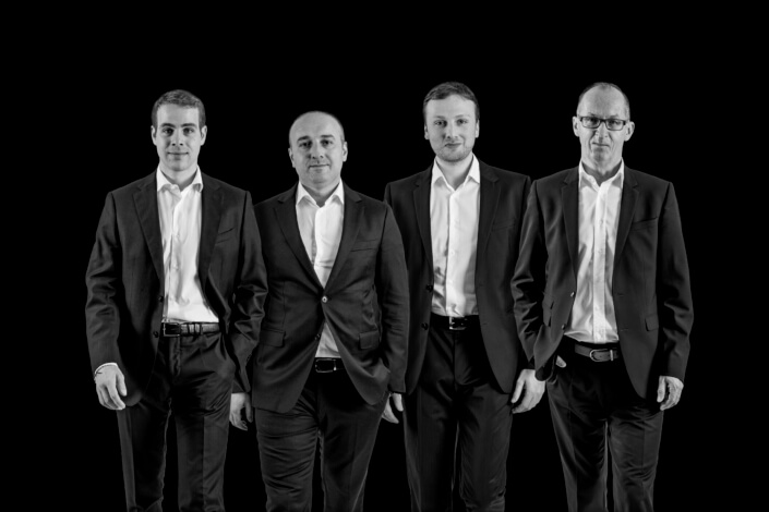 A group of men in suits pose in front of a black background.