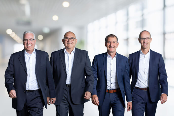 Four men in business suits stand together.