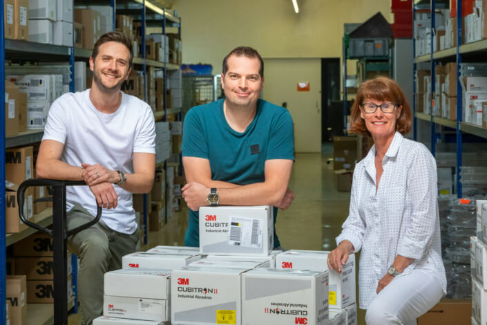 Three people pose in front of crates in a warehouse.