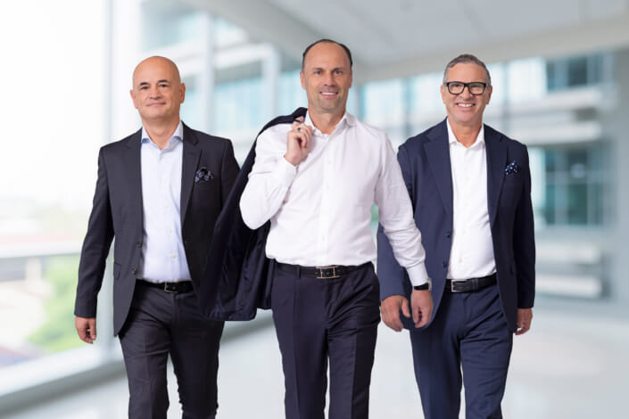 Three men in business suits walk through an office.