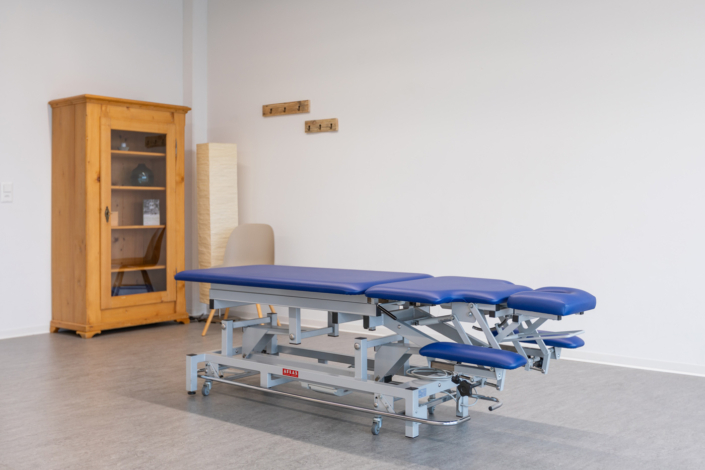 A blue massage table in a room with a cupboard.
