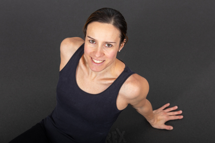 A woman in a black tank top poses in front of a gray background.