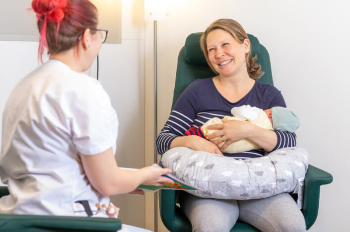 A woman holds a baby in a green chair.