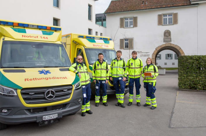 A group of people stand next to a Mercedes ambulance.