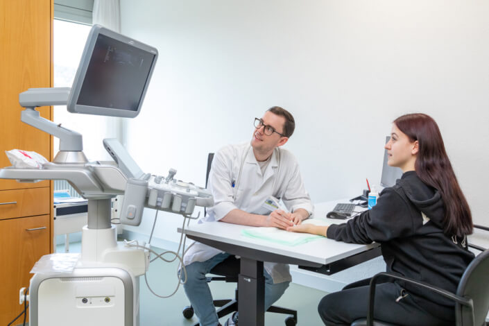 A woman and a man are sitting at a desk in a doctor's office.