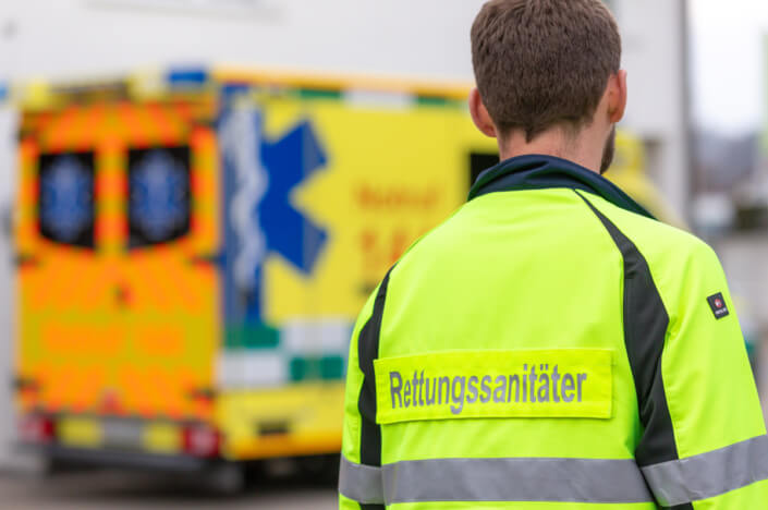 Ein Mann in einer gelben Jacke steht vor einem Krankenwagen.