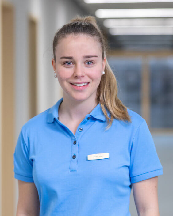 A person with a ponytail and a blue polo shirt is standing in a corridor.