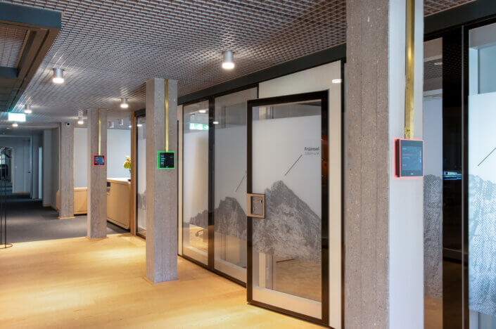 Modern office corridor with frosted glass doors, mountain pictures, digital signage on the walls and wooden floor.