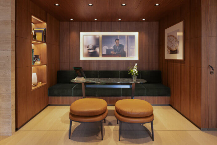 Small, wood-paneled sitting area with glass table, two brown leather stools and framed photos on the walls.