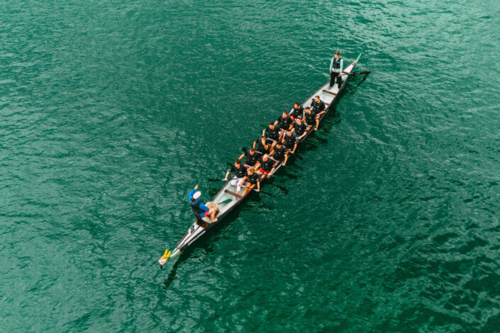 Luftaufnahme eines Drachenboots mit einer Gruppe von Menschen, die im türkisfarbenen Wasser rudern.