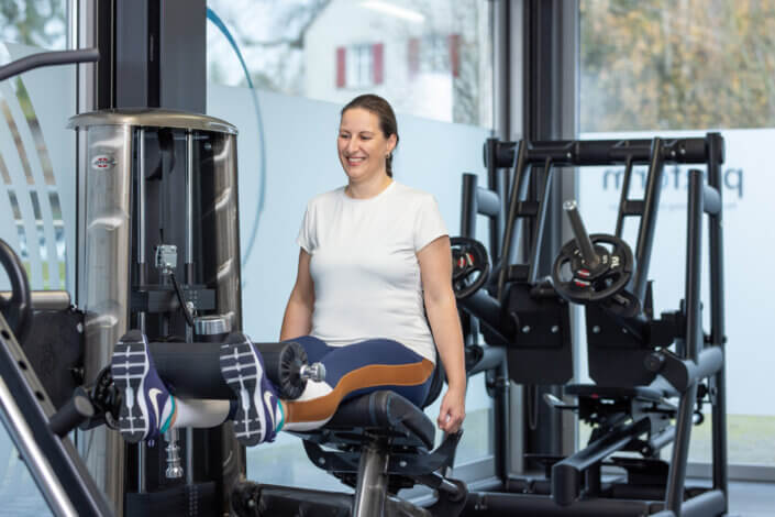 Person in a white shirt using a leg extension machine in a gym with exercise equipment in the background.