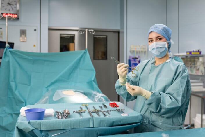 A doctor in surgical clothing holds an instrument in an operating theater; surgical instruments lie on a covered table.